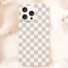 A Beige Phone Case With A Checkered Pattern Sits On A Peach-Colored Fabric.