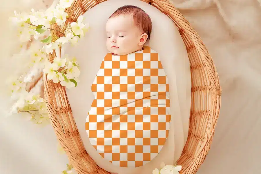 Sleeping baby swaddled in an orange and white checkered blanket.