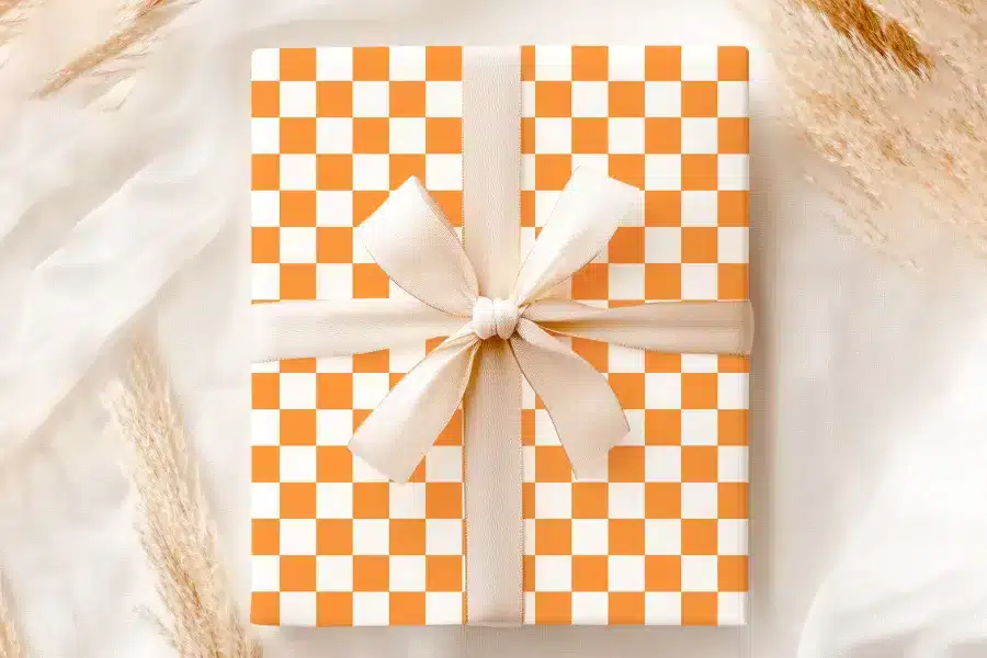 A Gift Box With An Orange And White Checkered Pattern, Tied With A Cream-Colored Ribbon.
