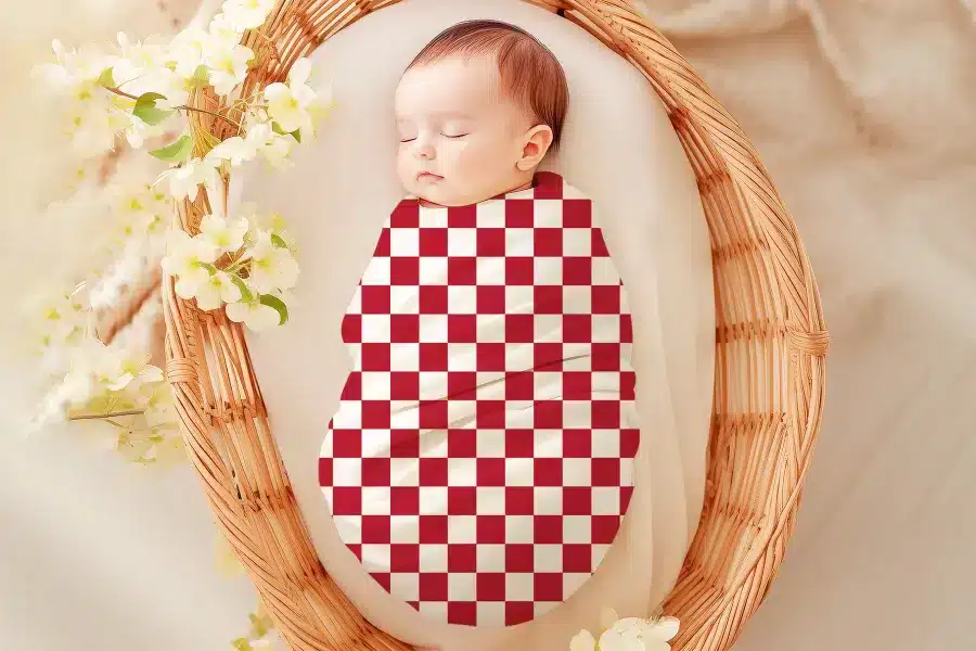 Sleeping baby swaddled in a red and white checkered receiving blanket.