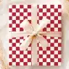 A Gift Wrapped In Red And White Checkered Paper With A Beige Ribbon.