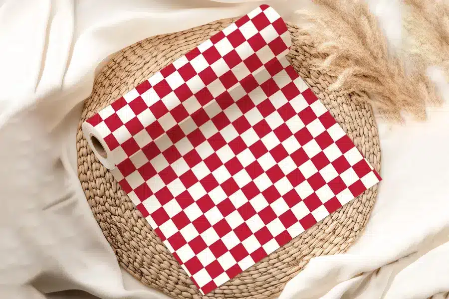 A Roll Of Red And White Checkered Paper Sits On A Woven Placemat.