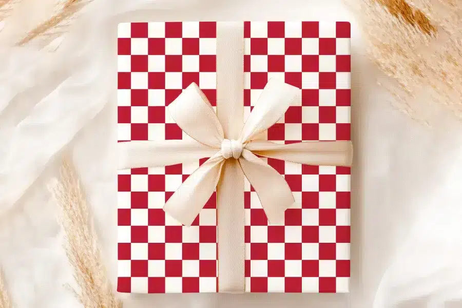A Gift Wrapped In Red And White Checkered Paper With A Beige Ribbon.