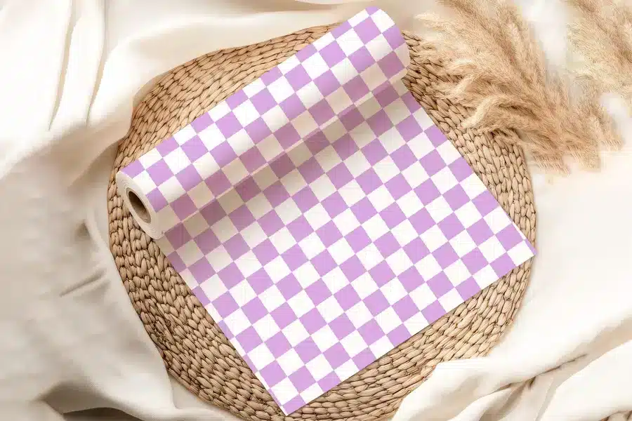 A Roll Of Lavender And White Checkered Wrapping Paper On A Woven Placemat.