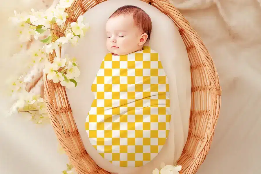 Sleeping baby swaddled in a yellow and white checkered blanket.