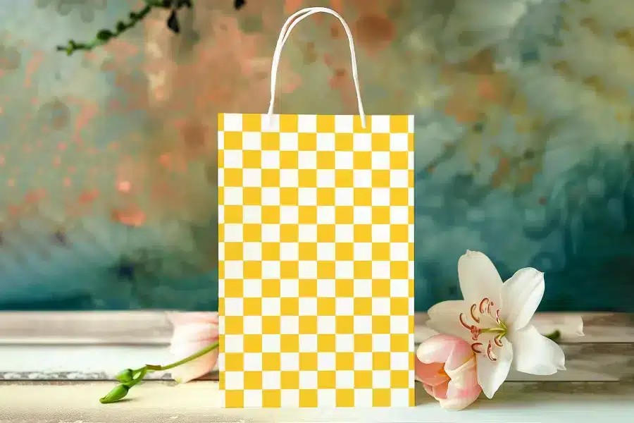 Yellow Checkered Paper Shopping Bag On A Table With Flowers.
