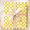A Gift Wrapped In Yellow And White Checkered Paper With A Beige Ribbon.