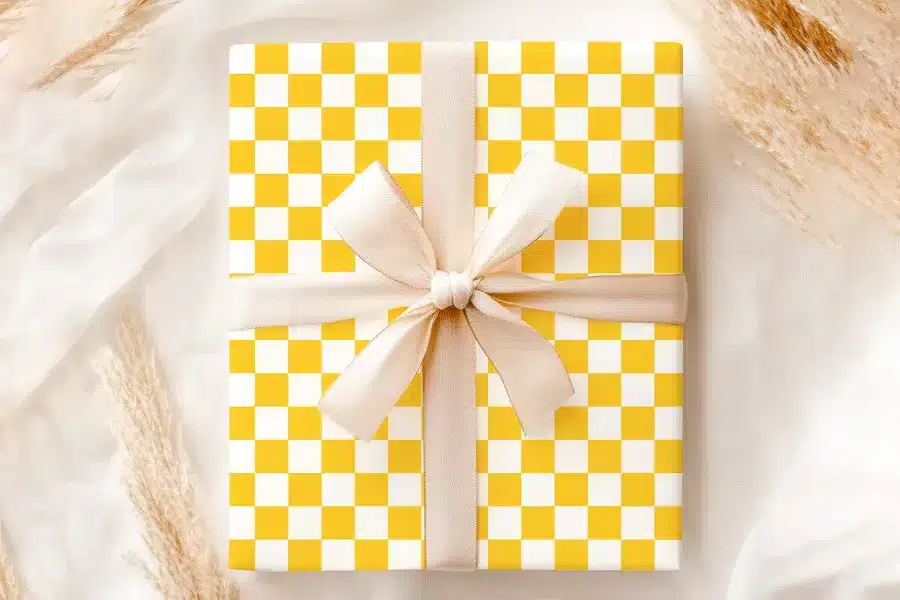A Gift Wrapped In Yellow And White Checkered Paper With A Beige Ribbon.