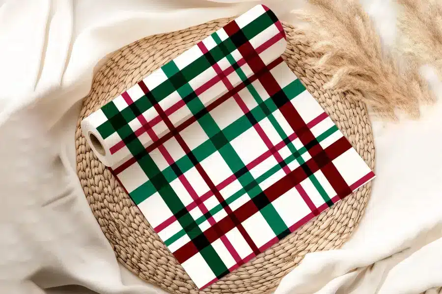 Roll Of Red, Green, And Black Plaid Wrapping Paper On A Woven Placemat.