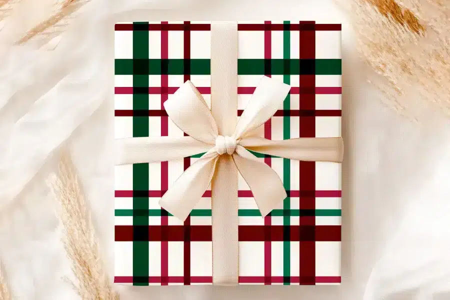 A Gift Wrapped In Cream-Colored Paper With A Red, Green, And Black Plaid Pattern And Tied With A Beige Ribbon.