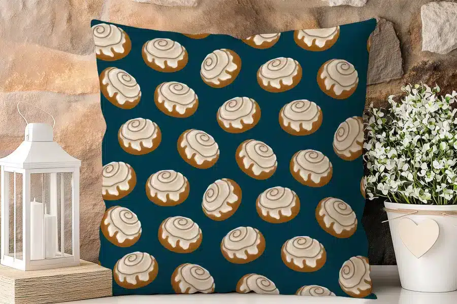 Teal Square Pillow With A Repeating Pattern Of Cinnamon Rolls.