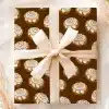 A Gift Wrapped In Brown Paper Featuring A Repeating Pattern Of Cinnamon Rolls, Tied With A Beige Ribbon.