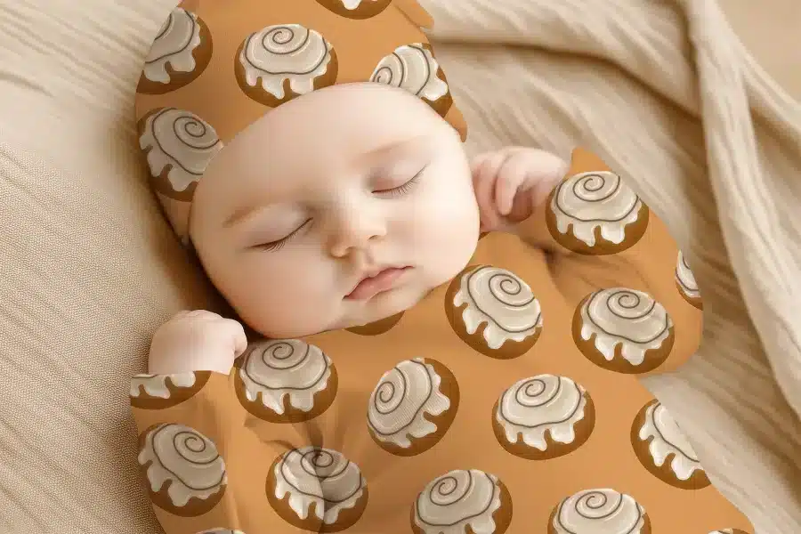Sleeping Baby Wearing A Cinnamon Roll Patterned Onesie And Hat.
