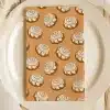 A Tan Napkin With A Repeating Pattern Of Cinnamon Rolls On A White Plate.