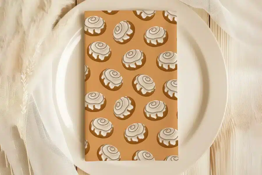 A Tan Napkin With A Repeating Pattern Of Cinnamon Rolls On A White Plate.