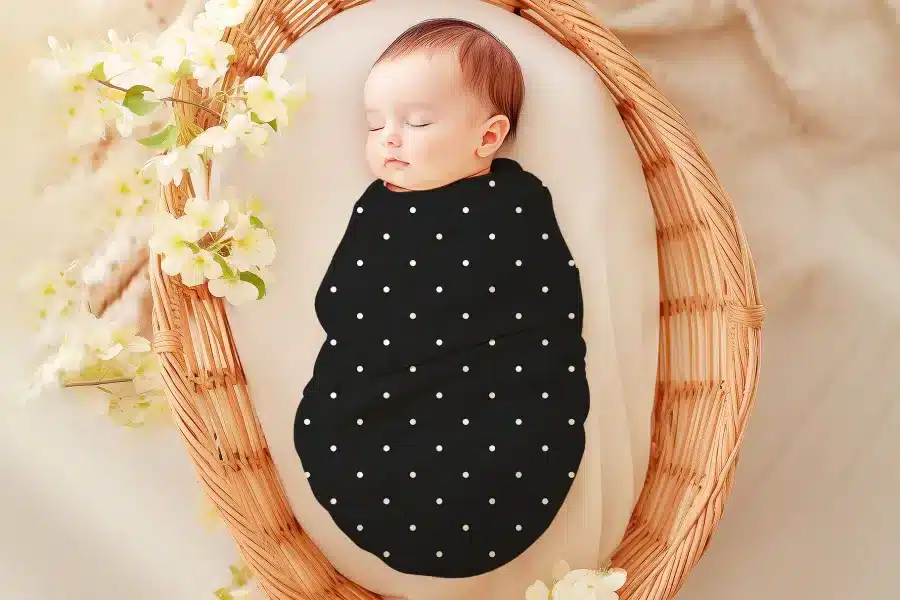 Sleeping baby swaddled in a black and white polka dot wrap.