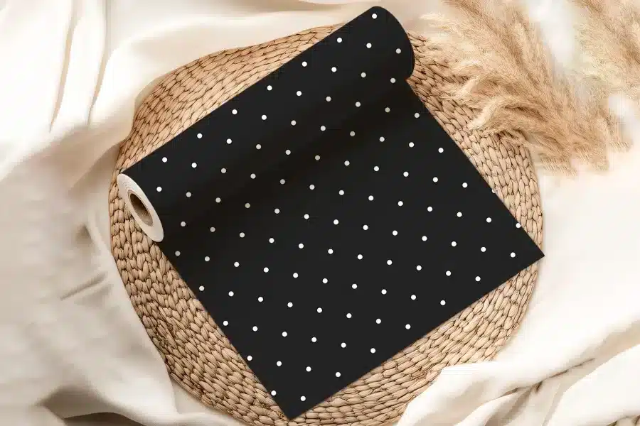 Black Fabric Roll With Small White Polka Dots, Resting On A Woven Placemat.