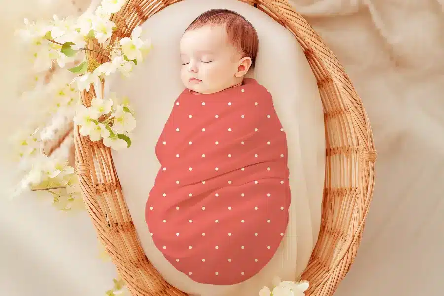 Sleeping baby swaddled in a coral-colored, white polka dot wrap.