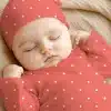 Sleeping Baby Wearing A Coral-Colored Polka Dot Onesie And Matching Hat.