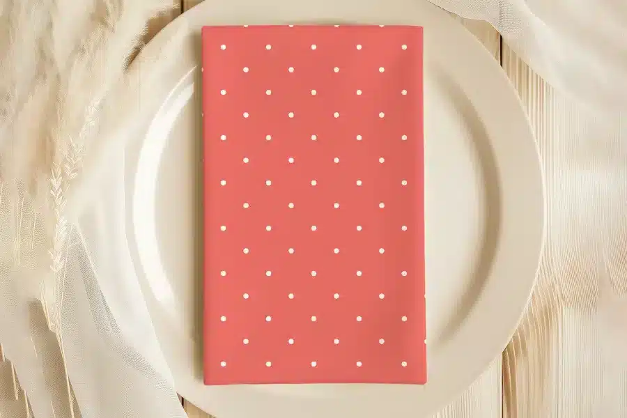 Coral-Colored Napkin With White Polka Dots On A White Plate.