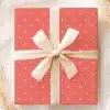 A Coral-Colored Gift Box With White Polka Dots, Tied With A Cream-Colored Ribbon And Bow.