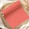 Coral-Colored Wrapping Paper With White Polka Dots, Rolled And Displayed On A Woven Mat.
