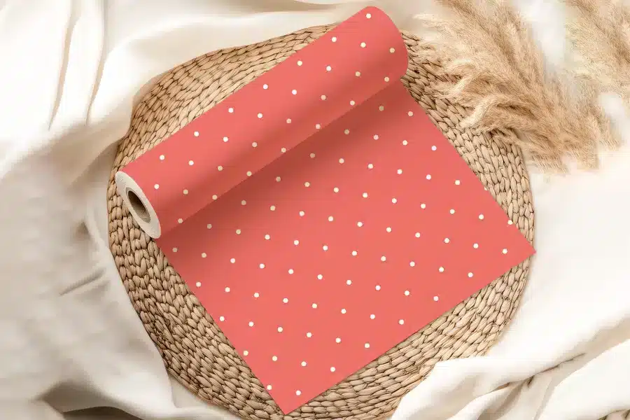 Coral-Colored Wrapping Paper With White Polka Dots, Rolled And Displayed On A Woven Mat.