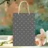Gray Gift Bag With White Polka Dots, Sitting On A Table With Pink And White Flowers.