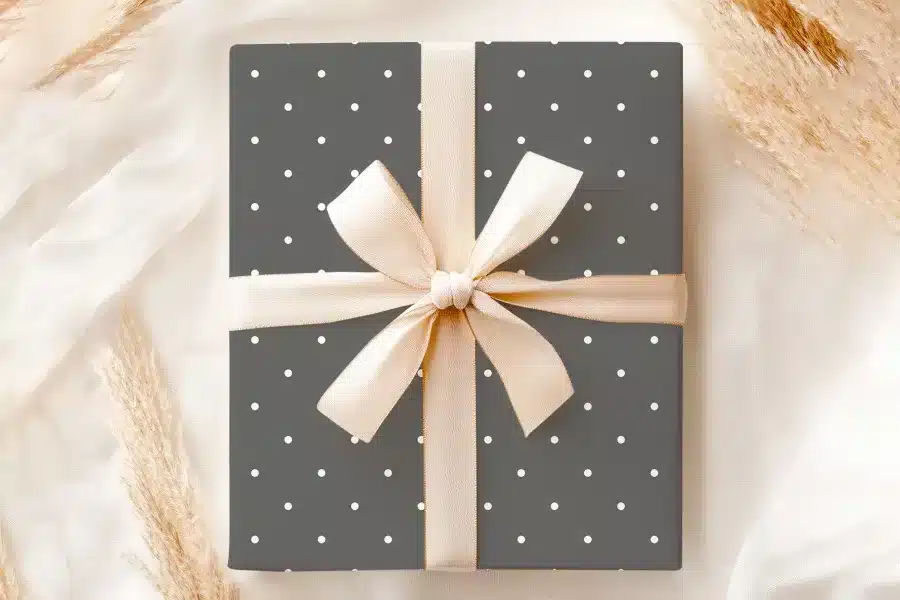A Gray Gift Box With White Polka Dots And A Beige Ribbon.