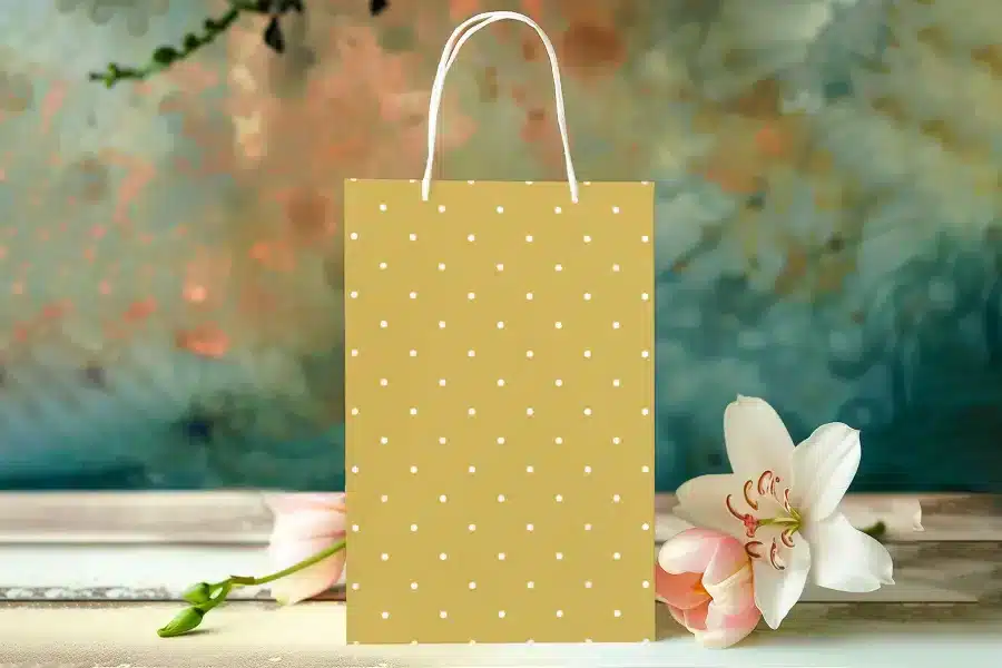 Mustard Yellow Gift Bag With White Polka Dots, Next To Pink Tulips And A White Lily.