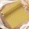 Mustard Yellow Wrapping Paper With White Polka Dots, Rolled On A Woven Mat.