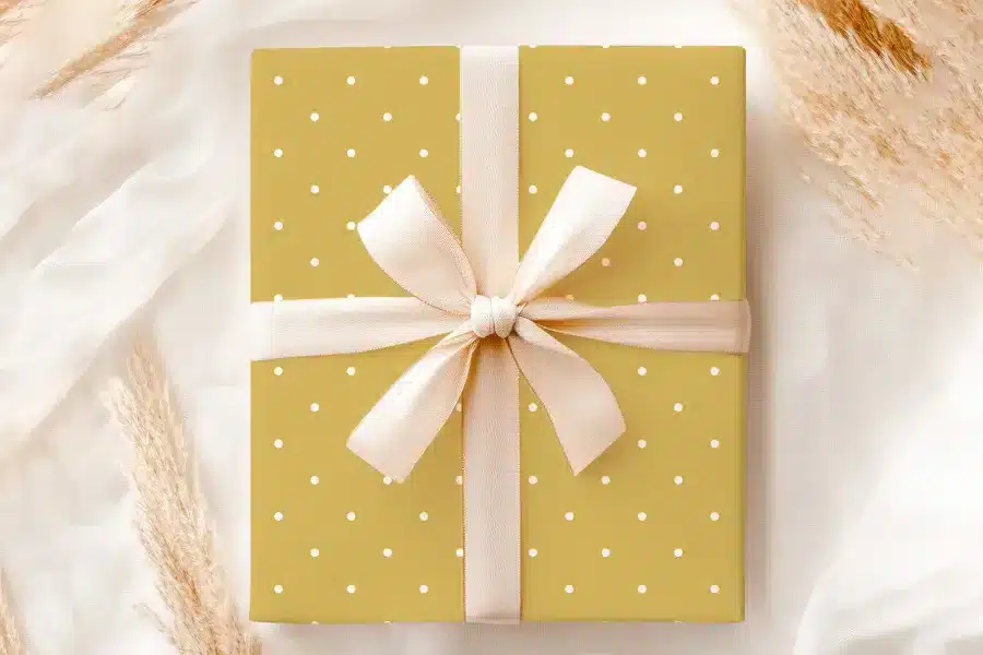 A Mustard Yellow Gift Box With White Polka Dots, Tied With A Cream-Colored Ribbon.