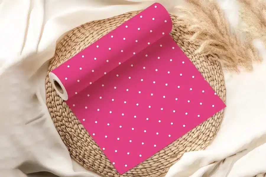 Pink Wrapping Paper Roll With White Polka Dots, Partially Unrolled On A Woven Placemat.