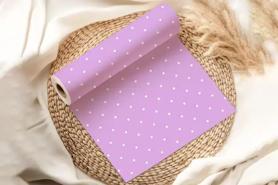 A Roll Of Lavender Wrapping Paper With White Polka Dots Rests On A Woven Placemat.