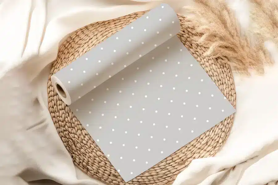 Grey Wrapping Paper With White Polka Dots, Rolled And Partially Unfurled On A Woven Mat.