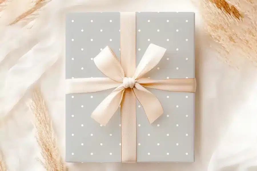 A Gray Gift Box With White Polka Dots And A Beige Ribbon.