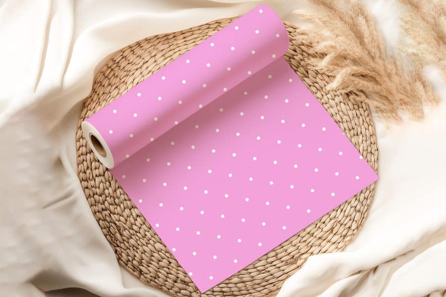 Pink Wrapping Paper With White Polka Dots, Rolled And Partially Unfurled, Sits On A Woven Mat.