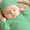 Sleeping Baby Wearing A Mint Green Polka Dot Outfit And Matching Hat.