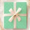 A Light Green Gift Box With White Polka Dots And A Beige Ribbon.