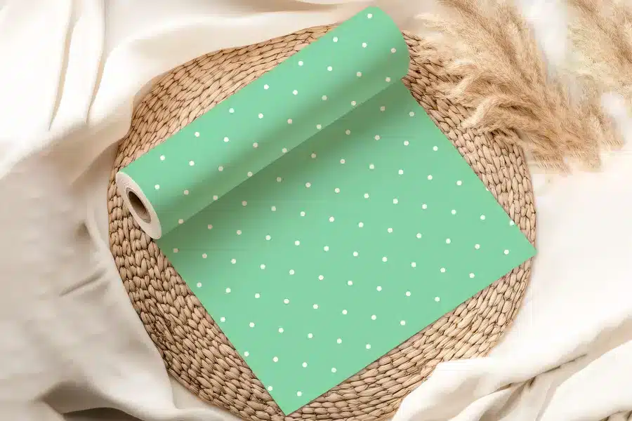 A Roll Of Light Green Wrapping Paper With White Polka Dots Is Partially Unrolled On A Woven Placemat.