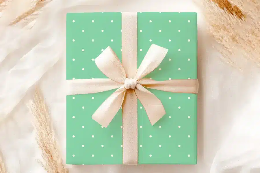 A Light Green Gift Box With White Polka Dots And A Beige Ribbon.