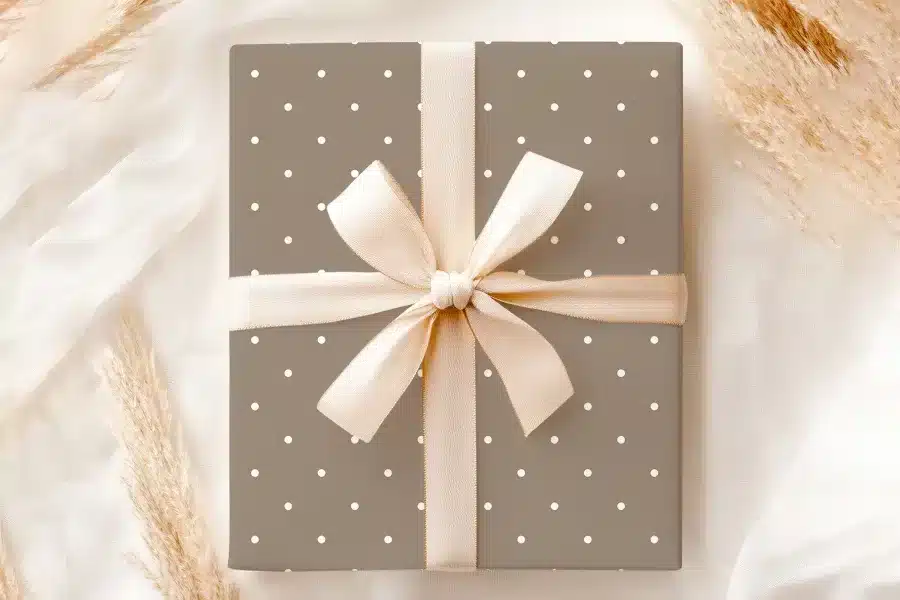 A Taupe Gift Box With White Polka Dots And A Beige Ribbon Tied In A Bow.
