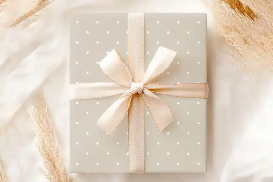 A Light Beige Gift Box With White Polka Dots And A Beige Ribbon Tied In A Bow.