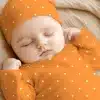 Sleeping Baby Wearing An Orange Polka Dot Onesie And Matching Hat.