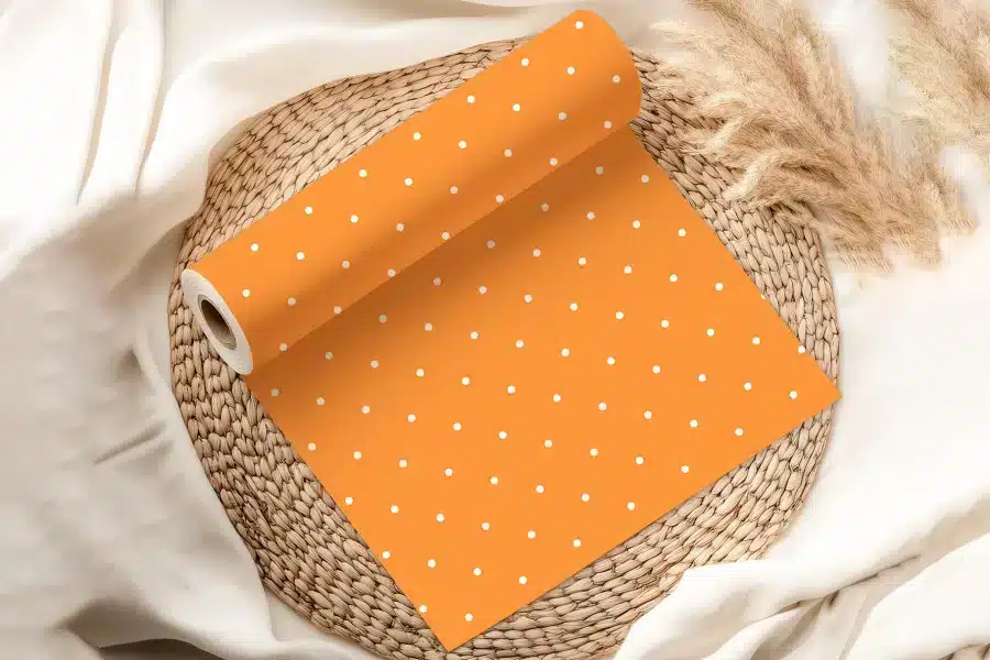 Orange Wrapping Paper With White Polka Dots, Partially Unrolled On A Woven Mat.
