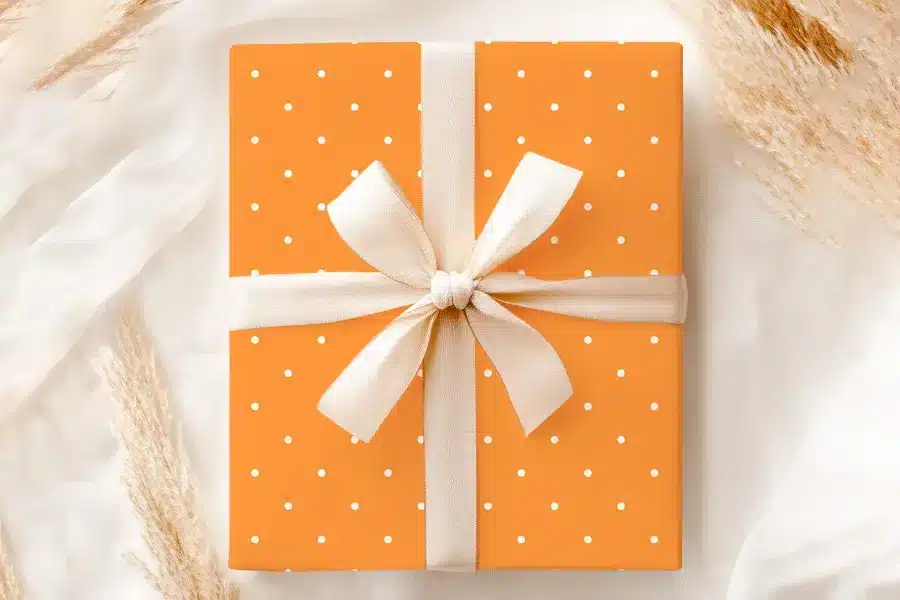 An Orange Gift Box With White Polka Dots And A Cream-Colored Ribbon.