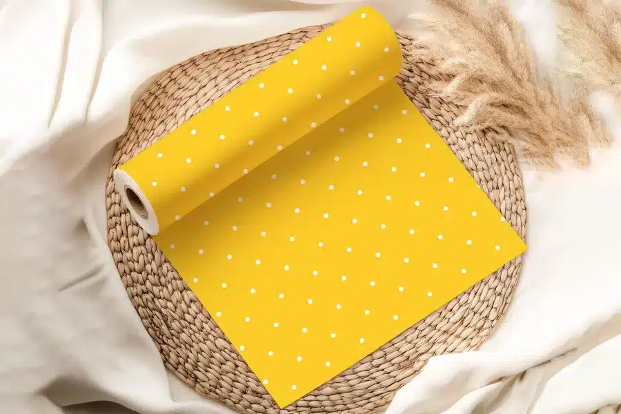 A Roll Of Yellow Wrapping Paper With White Polka Dots, Partially Unrolled On A Woven Placemat.
