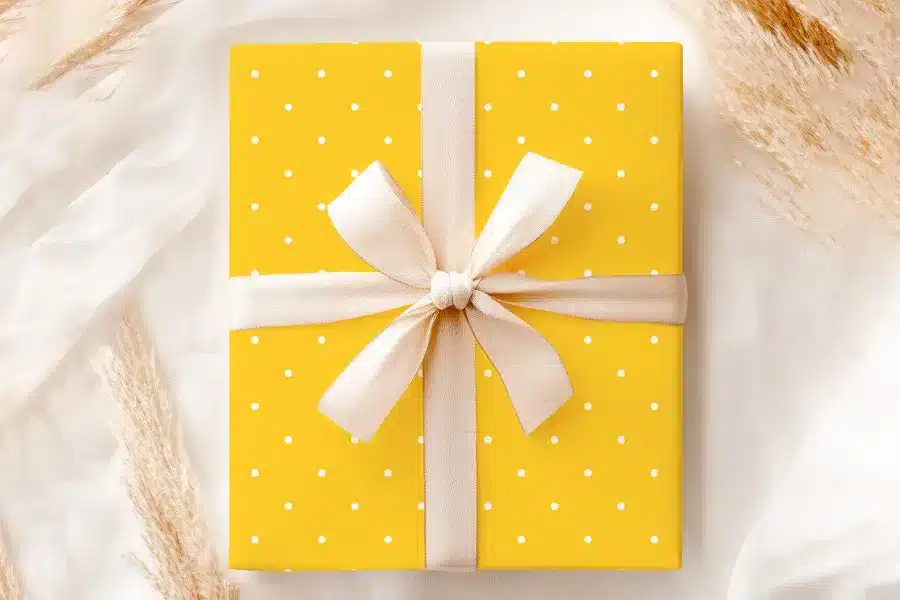 A Yellow Gift Box With White Polka Dots And A Beige Ribbon.