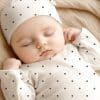 Sleeping Baby Wearing A White Polka Dot Onesie And Matching Hat.