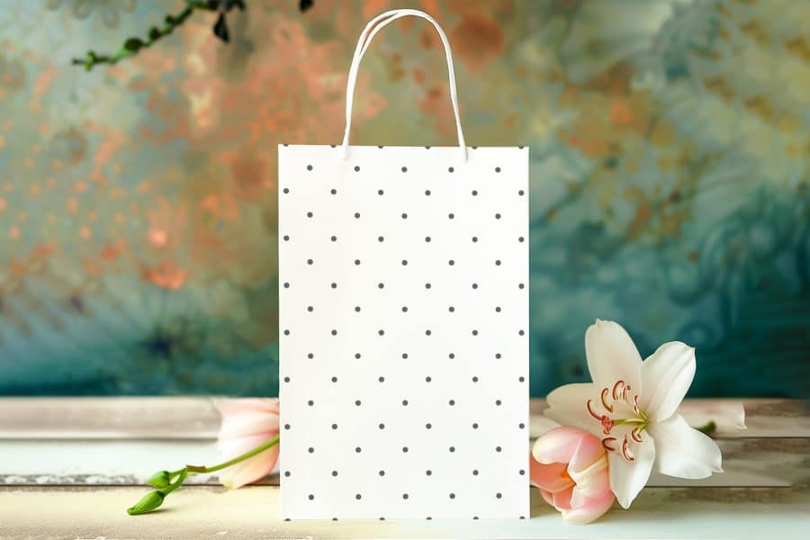 White Polka Dot Shopping Bag On A Table With Pink Flowers.